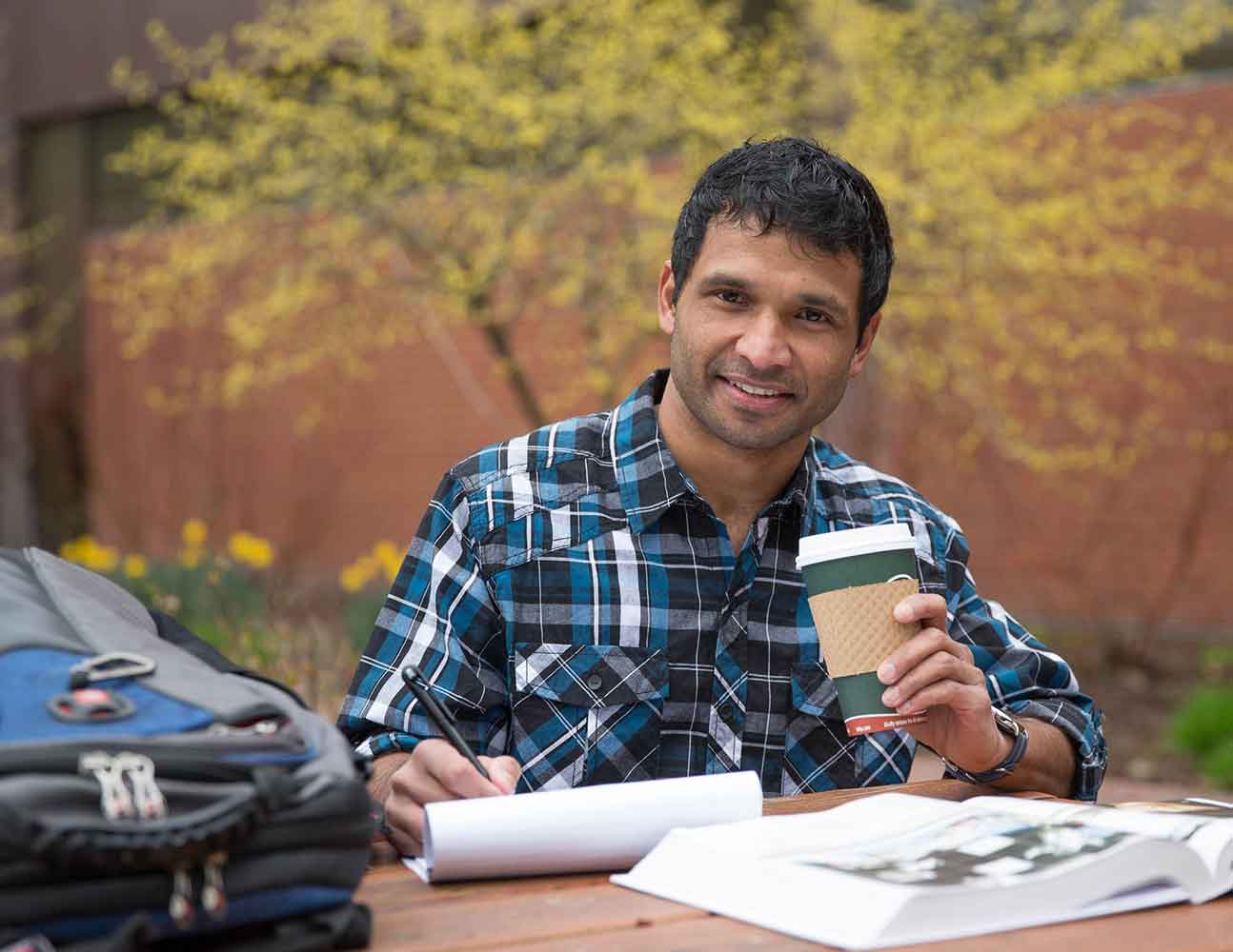 A student writes on a notepad while drinking coffee